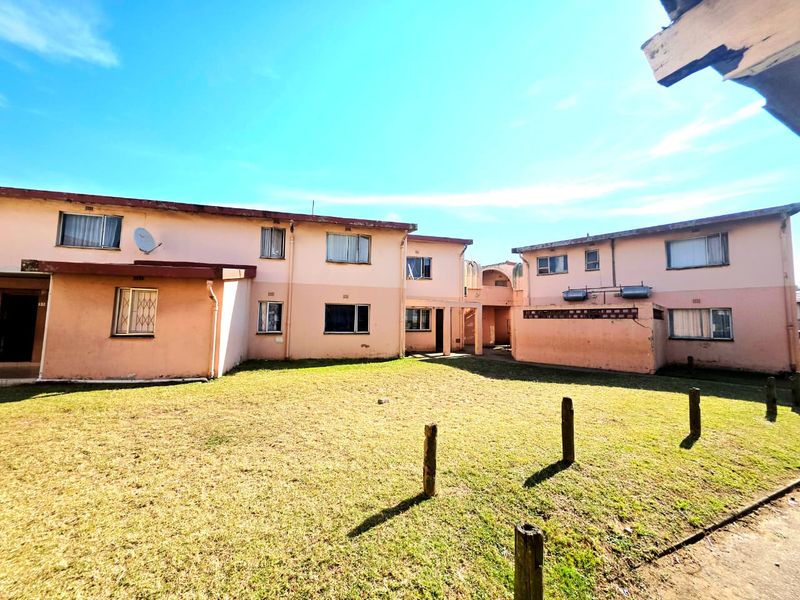Rear view of a multi-unit apartment complex featuring a shared lawn area, weathered exterior walls, and security bars on windows.