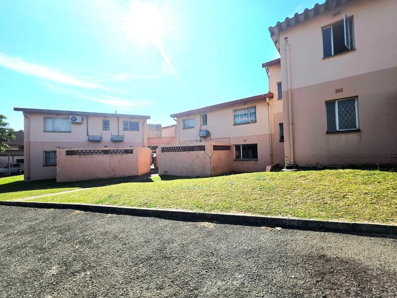 Exterior view of the apartment complex showing the rear facade, communal lawn area, and paved driveway access.