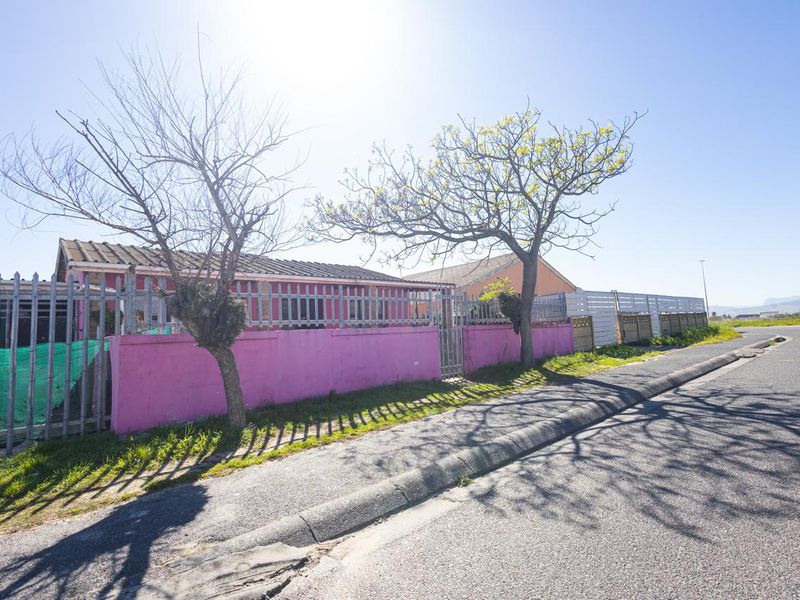 Street view of the property showing the front perimeter wall, security fencing, and tiled roof structure from the roadside.