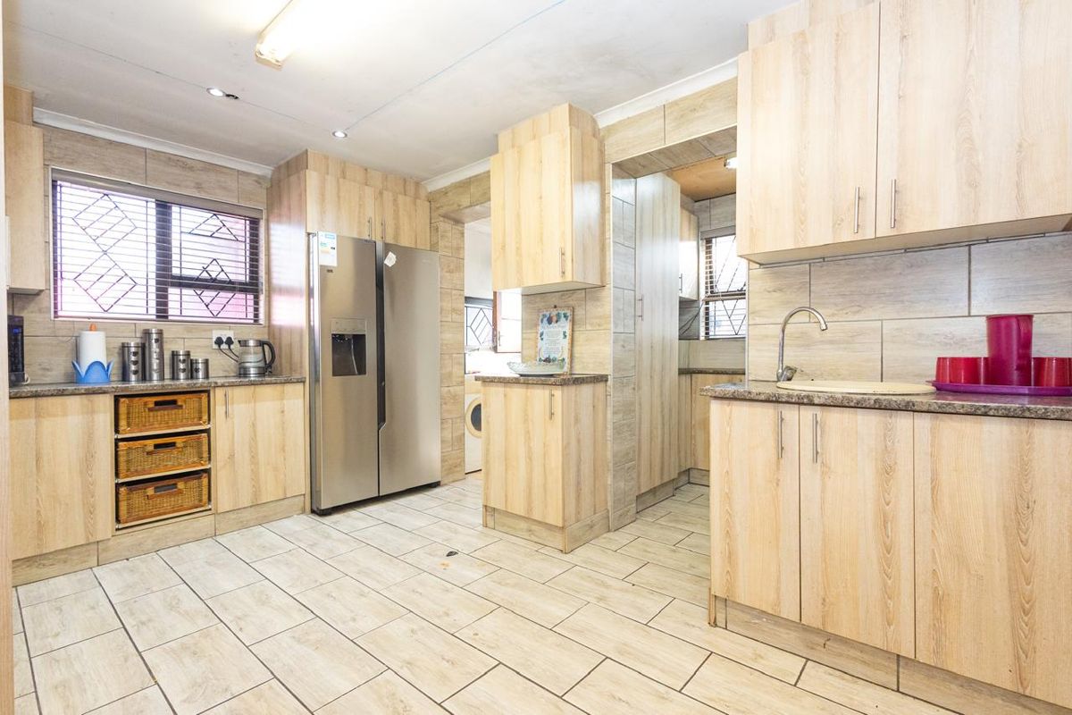 A functional kitchen featuring light wood-look cabinetry, stone-effect countertops, tiled flooring, and a tiled backsplash, with an adjacent scullery area.