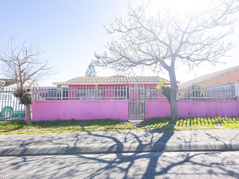Front view of a residential property featuring a pink perimeter wall, metal security fencing, and a tiled roof structure.