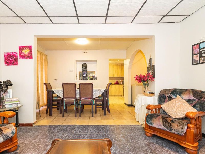 Open plan living and dining area featuring tiled floors, a drop ceiling, and an arched entryway leading to a functional kitchen space.
