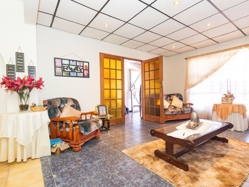 A living room featuring tiled flooring, a suspended ceiling with recessed lighting, and timber-framed glass doors leading to an adjacent space.