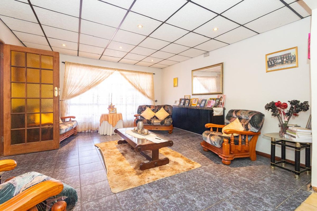 A spacious living room featuring tiled flooring and a suspended ceiling grid with recessed lighting, offering a functional layout for family relaxation.