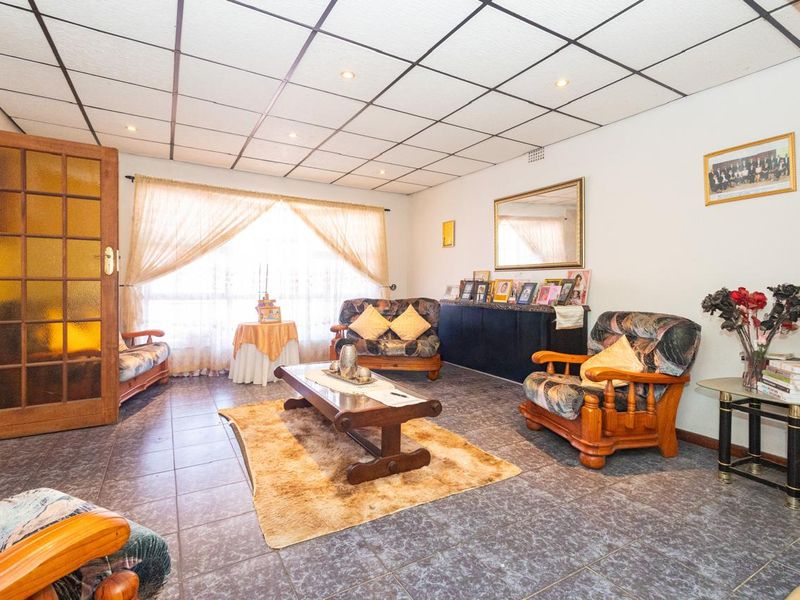 A spacious living room featuring tiled flooring and a suspended ceiling grid with recessed lighting, offering a functional layout for family relaxation.