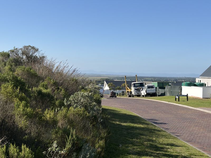 A view of a paved residential street and verge within a developed estate, showing surrounding landscape and nearby property infrastructure.
