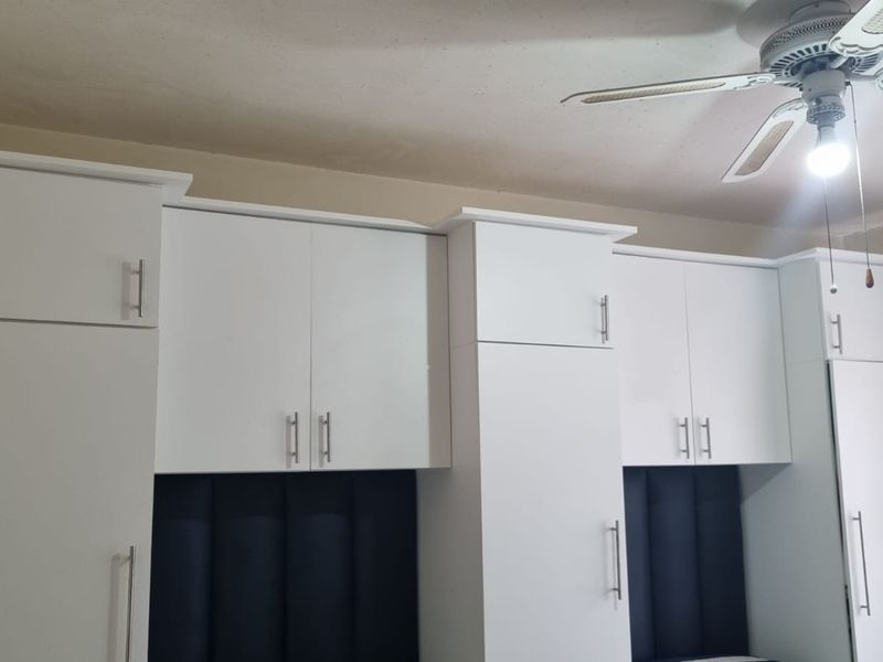 A bedroom featuring white built-in cupboards with modern handles and a ceiling fan.