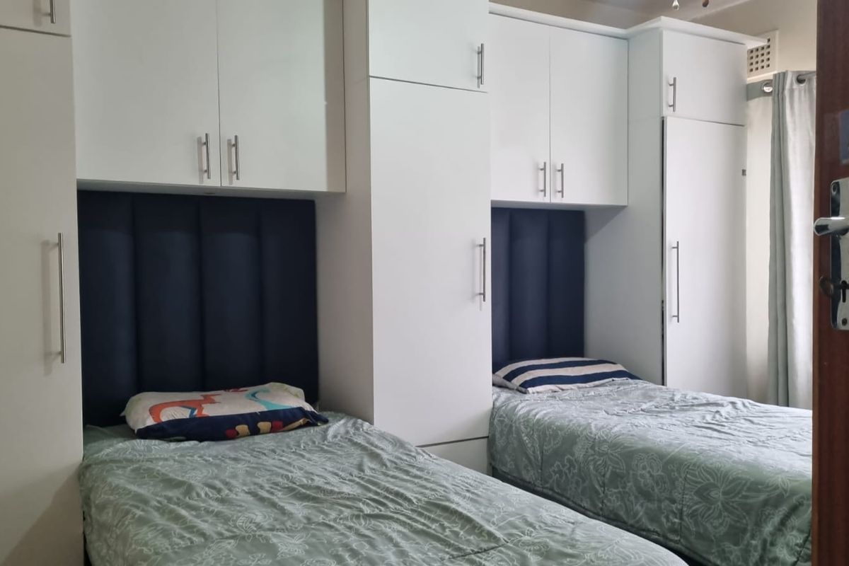 A bedroom featuring white built-in cupboards and integrated dark blue upholstered headboards for two single beds.