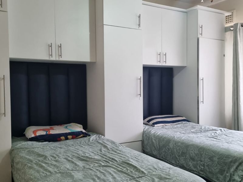 A bedroom featuring white built-in cupboards and integrated dark blue upholstered headboards for two single beds.
