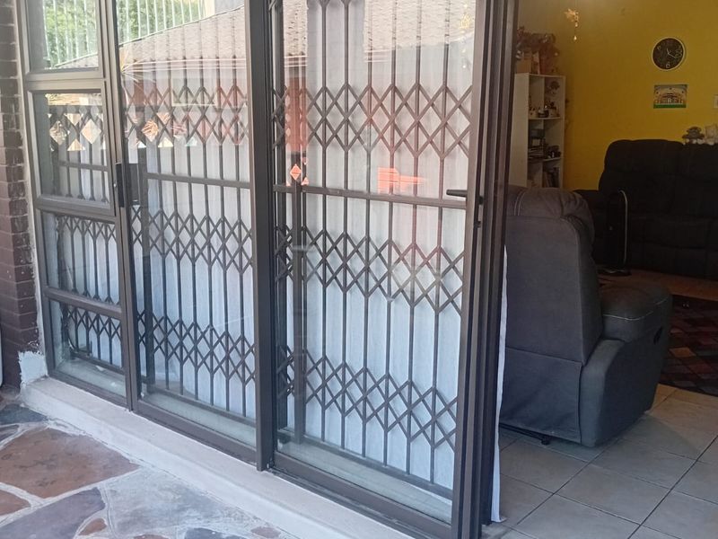 A covered patio area featuring stone paving and a sliding glass door with a security gate, providing access to the interior living space.