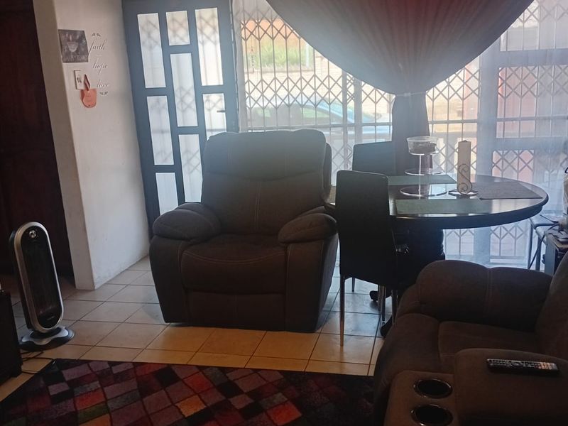 A living room area featuring tiled flooring, a wall-mounted air conditioning unit, and a security gate leading to the exterior.