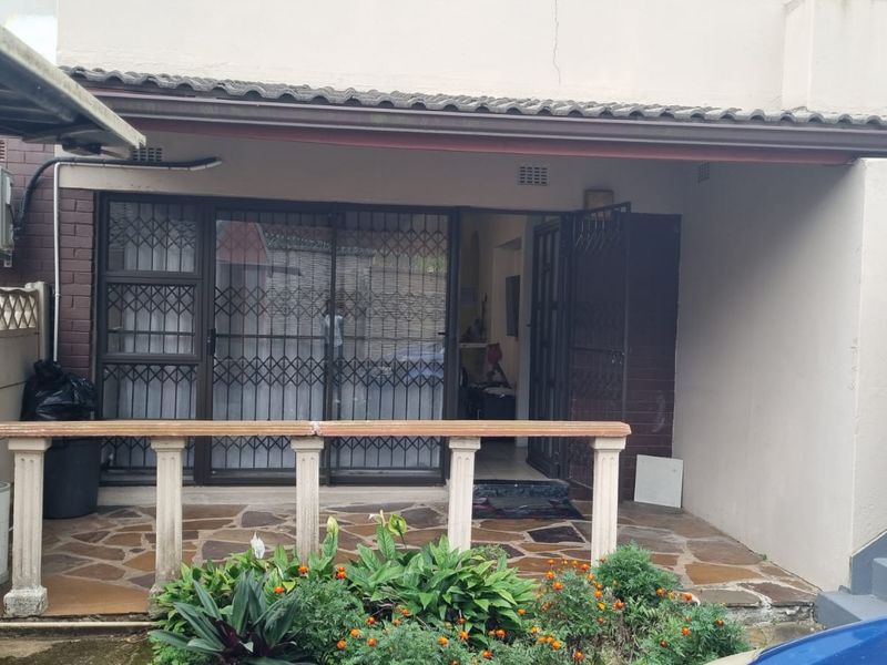 A covered patio area featuring stone paving, a concrete balustrade, and sliding glass doors with security gates, providing access to the townhouse interior.