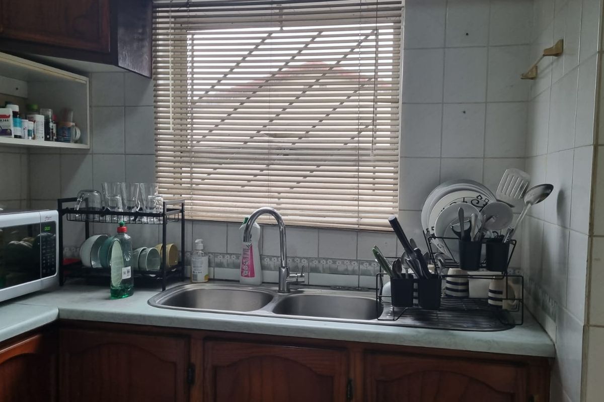 A functional kitchen area featuring timber cabinetry, a double bowl stainless steel sink, and tiled splashbacks, offering potential for modern cosmetic updates.