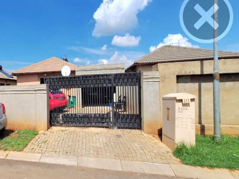 Front view of the property featuring a secure metal driveway gate, paved driveway, and perimeter walling.