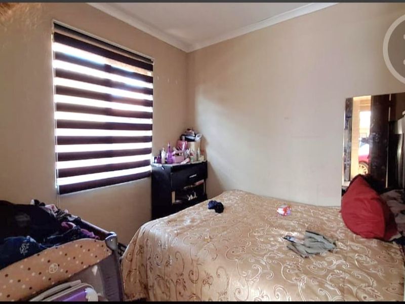 A standard bedroom featuring neutral wall finishes, a window with roller blinds, and a built-in mirror.