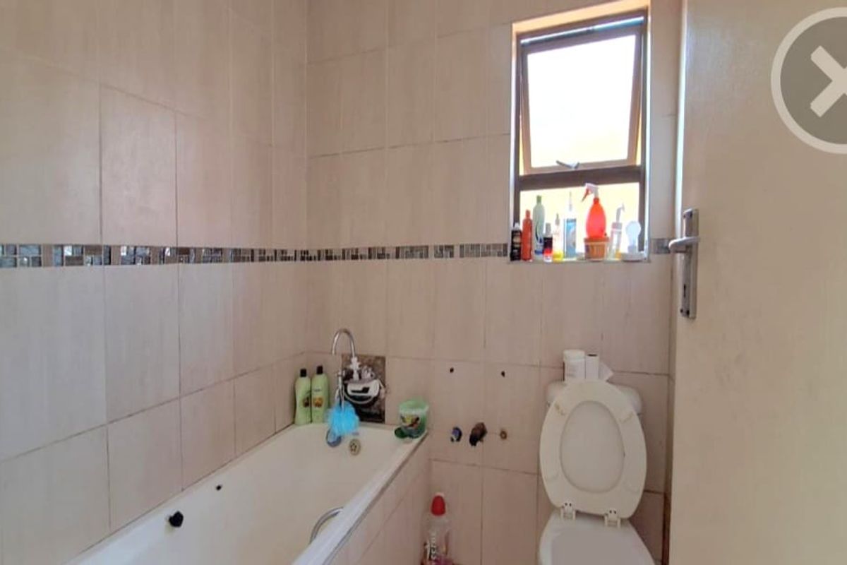 A functional bathroom featuring a bathtub, toilet, and tiled walls with a decorative mosaic border.