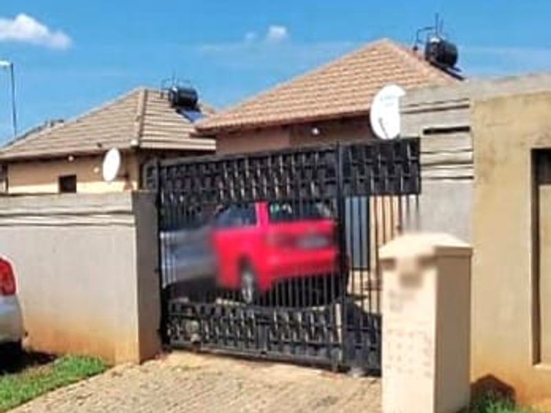 Front exterior view of a residential property featuring a tiled roof, solar water heater, perimeter wall, and a secure metal driveway gate.