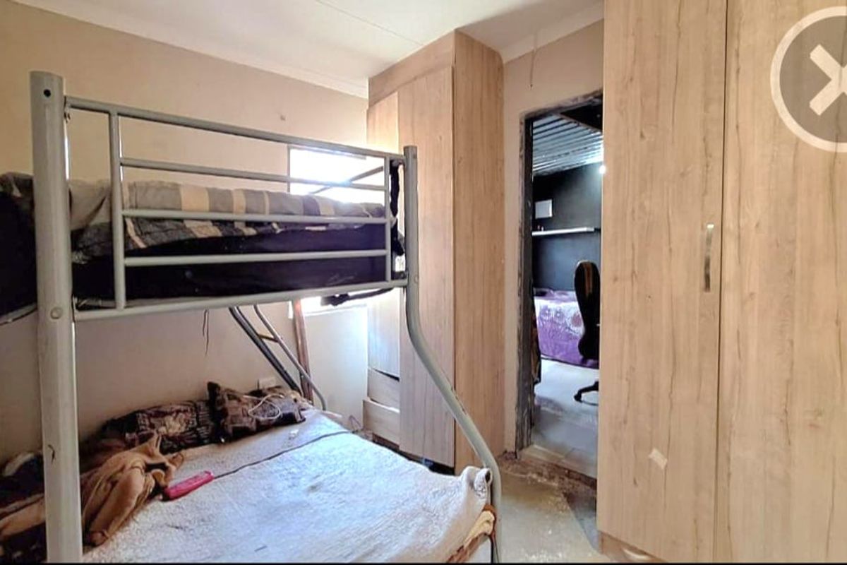 A bedroom featuring built-in wooden cupboards, with an unfinished doorway leading to an adjacent room and visible wear on the flooring.