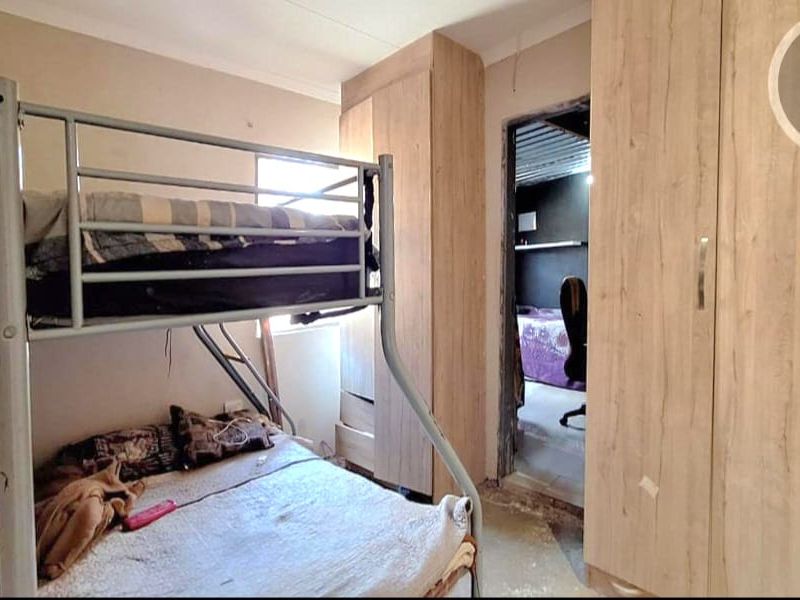 A bedroom featuring built-in wooden cupboards, with an unfinished doorway leading to an adjacent room and visible wear on the flooring.