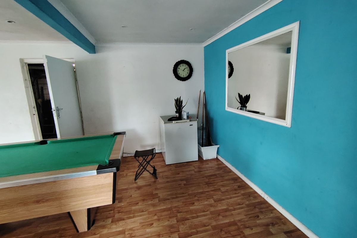 A multi-purpose living space featuring laminate flooring, recessed lighting, and a bold blue accent wall with a large mirror.