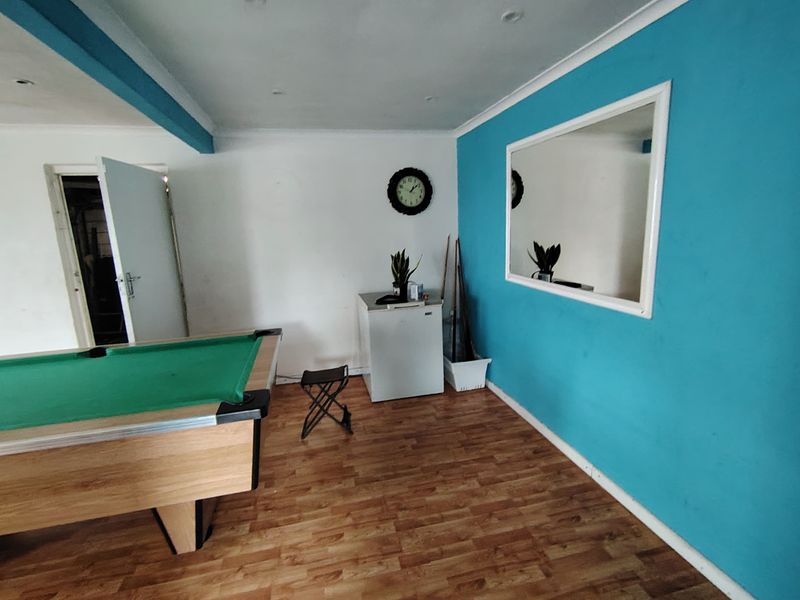 A multi-purpose living space featuring laminate flooring, recessed lighting, and a bold blue accent wall with a large mirror.