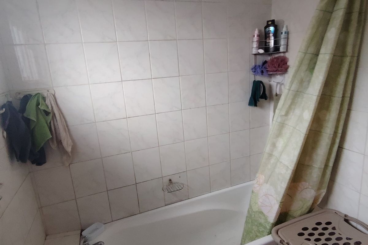 A functional bathroom featuring a built-in bathtub with shower attachment, tiled walls, and floor, requiring cosmetic updates to modernize the space.