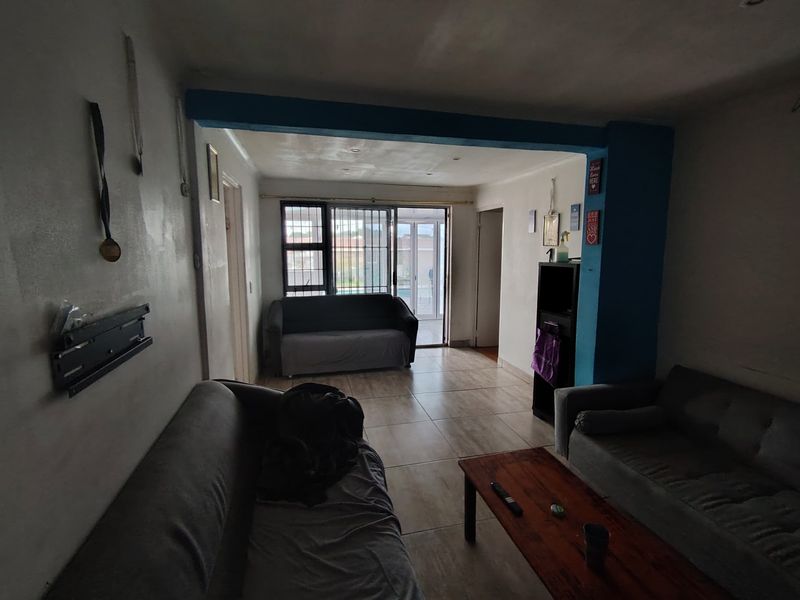 A living room featuring tiled flooring, a structural beam, and a sliding glass door with security bars leading to the exterior.