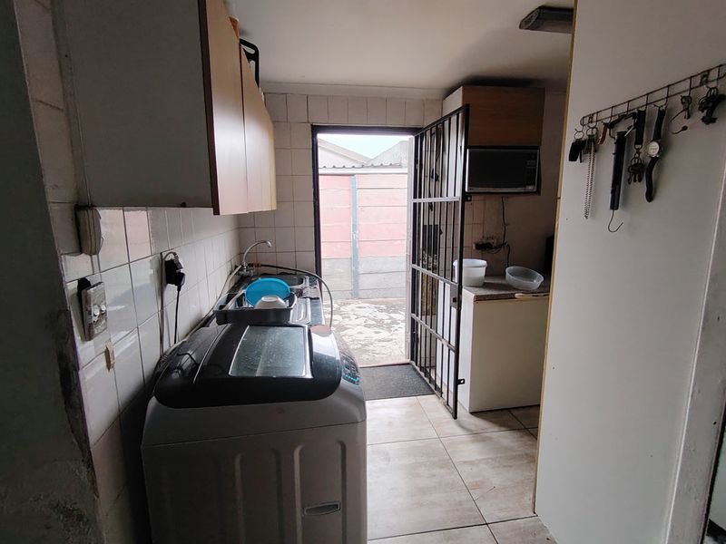 Functional laundry area featuring tiled walls, built-in cabinetry, and a sink, with direct access to the rear exterior through a security gate.