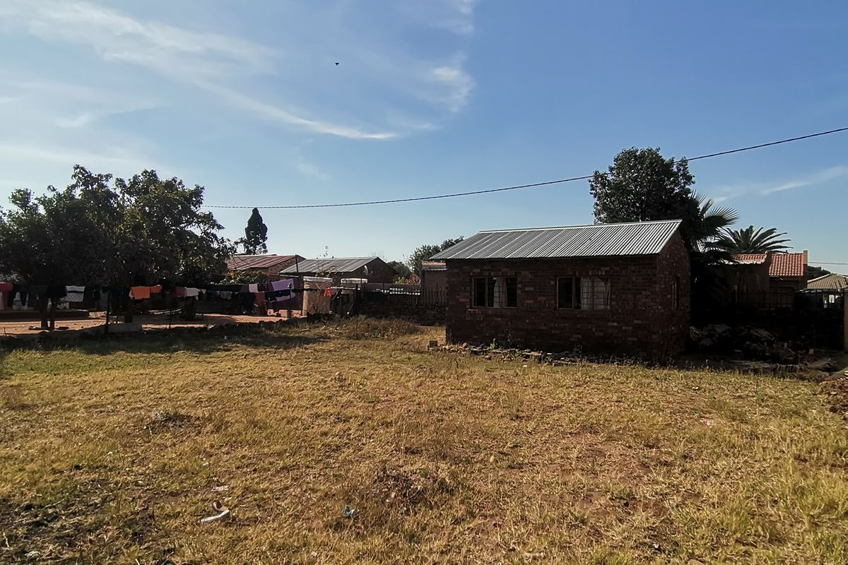 A view of a detached brick structure with a corrugated metal roof situated on a large, unlandscaped plot of land.