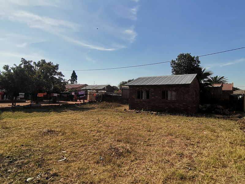 A view of a detached brick structure with a corrugated metal roof situated on a large, unlandscaped plot of land.