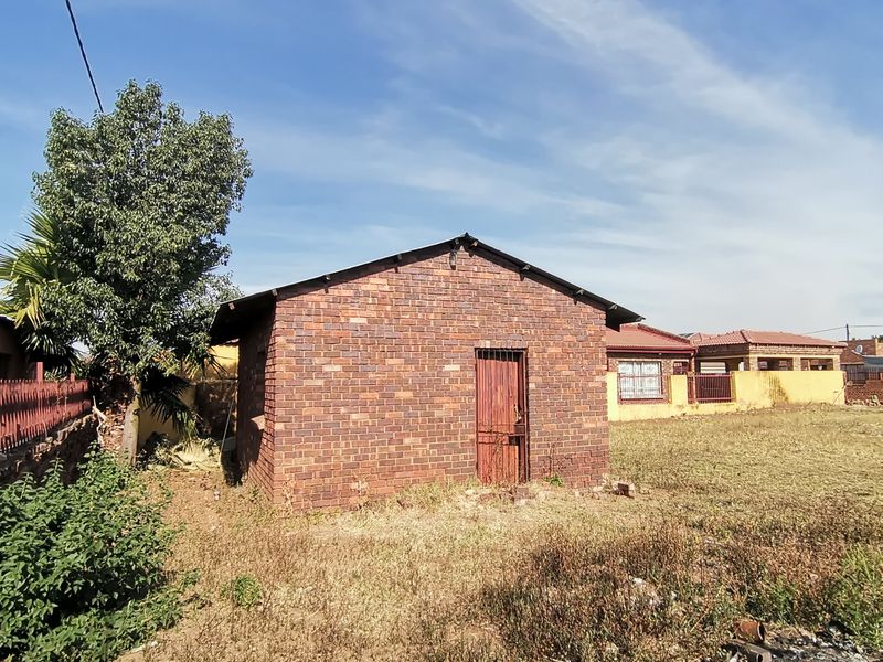 A detached brick outbuilding structure located in the rear yard, featuring a metal door and pitched roof, requiring significant maintenance and exterior improvements.