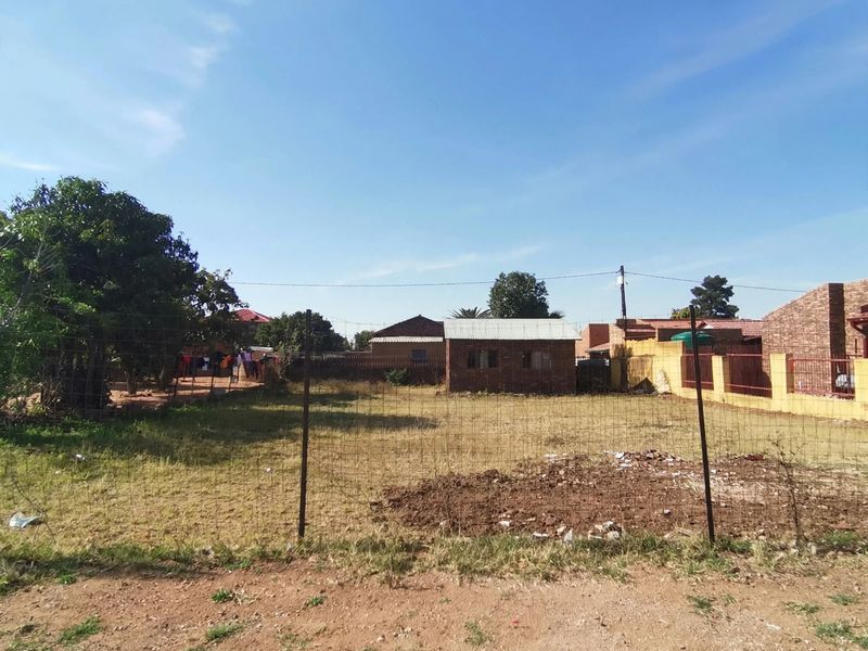 A view of the rear yard featuring a wire mesh fence, an outbuilding, and a brick boundary wall.