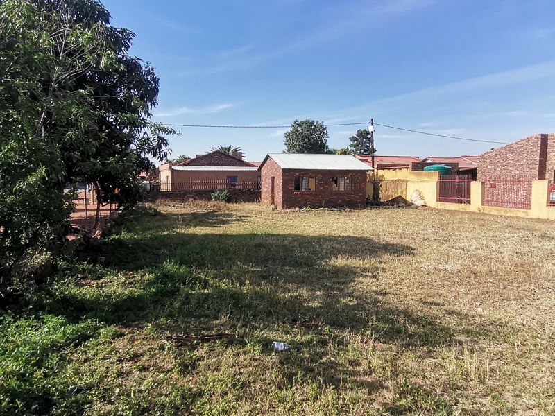 A spacious backyard area featuring a small brick outbuilding, perimeter boundary walls, and an expansive lawn requiring maintenance.