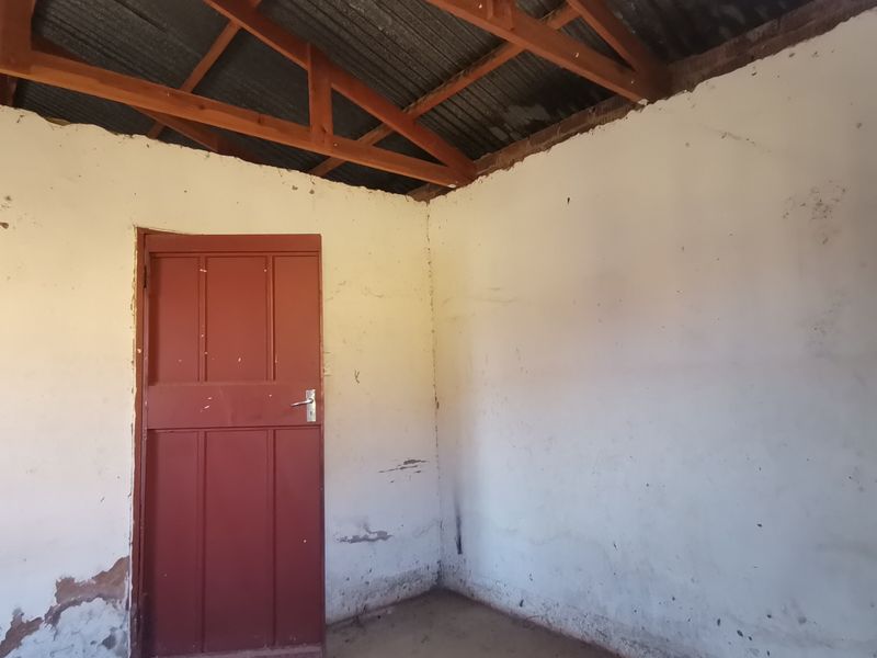 An unfinished interior room featuring exposed timber roof trusses, corrugated metal roofing, and a single timber door, requiring significant renovation and finishing.