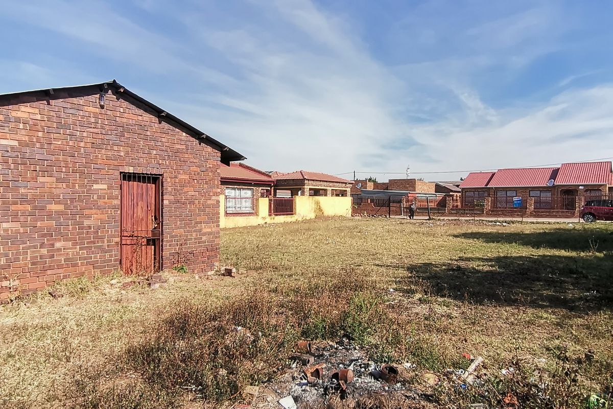 A view of the rear yard featuring a brick outbuilding, perimeter fencing, and an open grass area requiring landscaping.