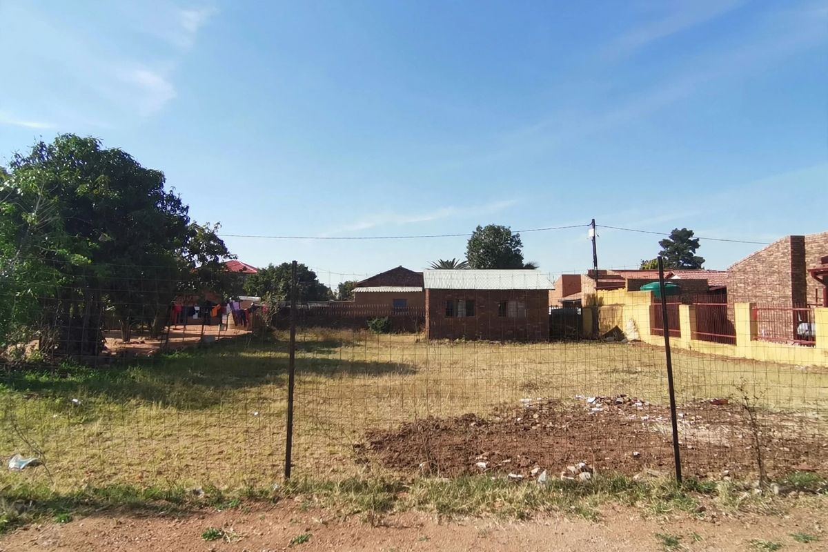 A view of the rear yard featuring a wire mesh fence, an outbuilding, and a brick boundary wall.