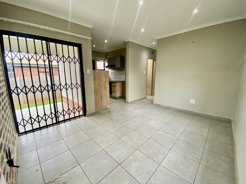 Open-plan living area featuring tiled floors, recessed lighting, and a compact kitchen with built-in cabinetry, leading to an outdoor patio through a security gate.