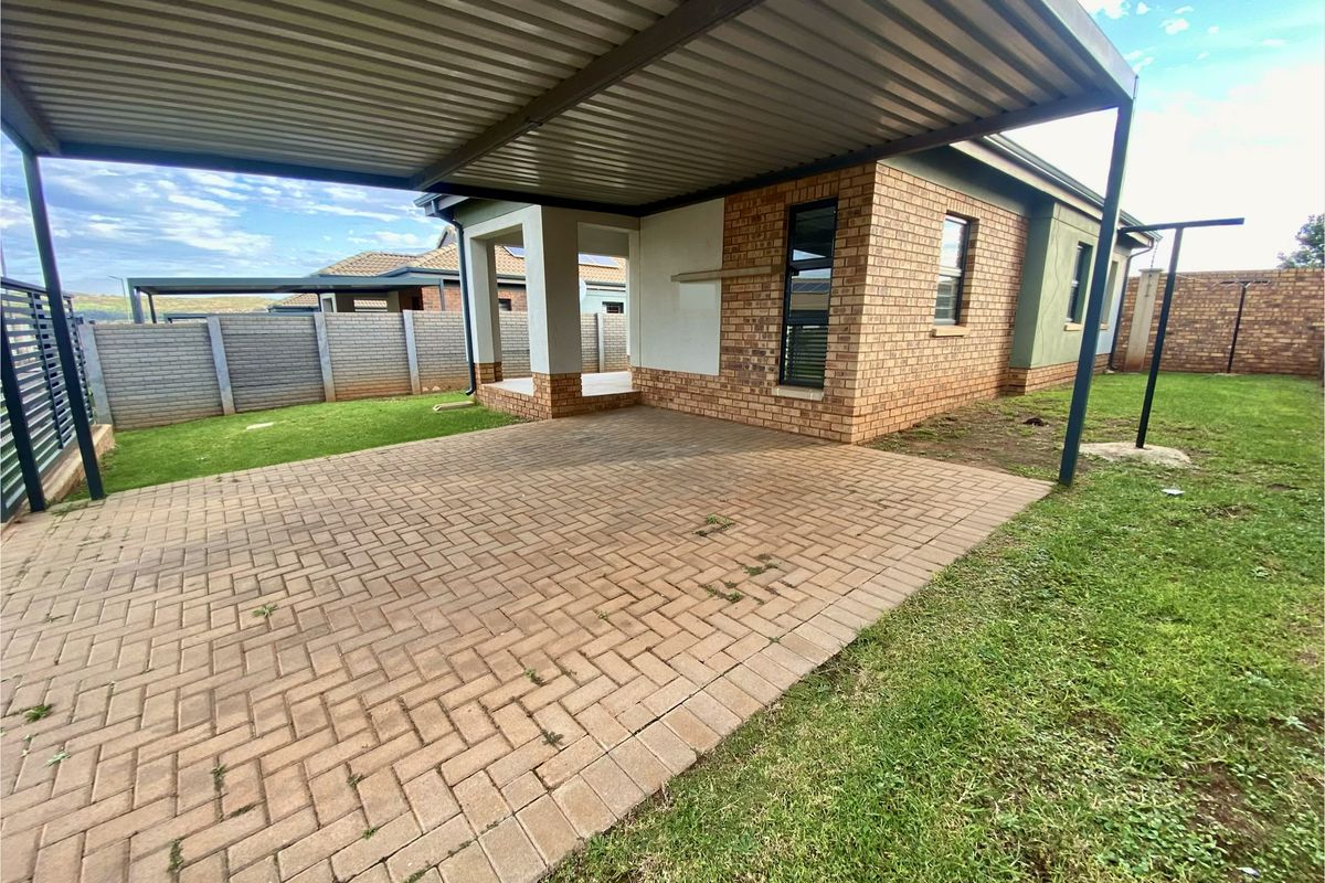 Rear exterior view featuring a paved driveway, covered carport, brick facade, and a surrounding lawn with boundary walling.
