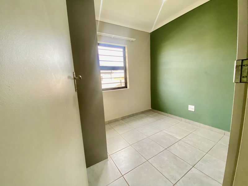 A clean, empty bedroom featuring tiled flooring, a window with security bars, and a green accent wall.