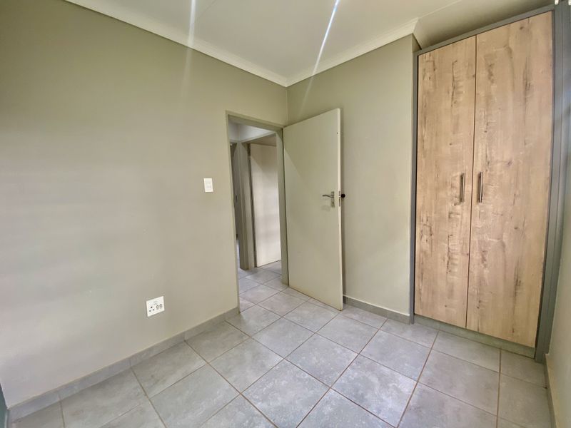 A clean, empty bedroom featuring neutral wall paint, tiled flooring, and a modern built-in wardrobe with wood-grain finish.