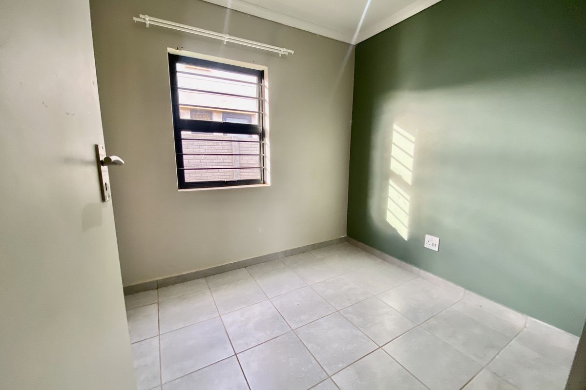 A clean, empty bedroom featuring neutral and green painted walls, tiled flooring, and a window fitted with security bars.