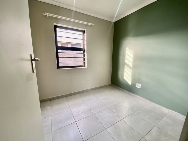 A clean, empty bedroom featuring neutral and green painted walls, tiled flooring, and a window fitted with security bars.