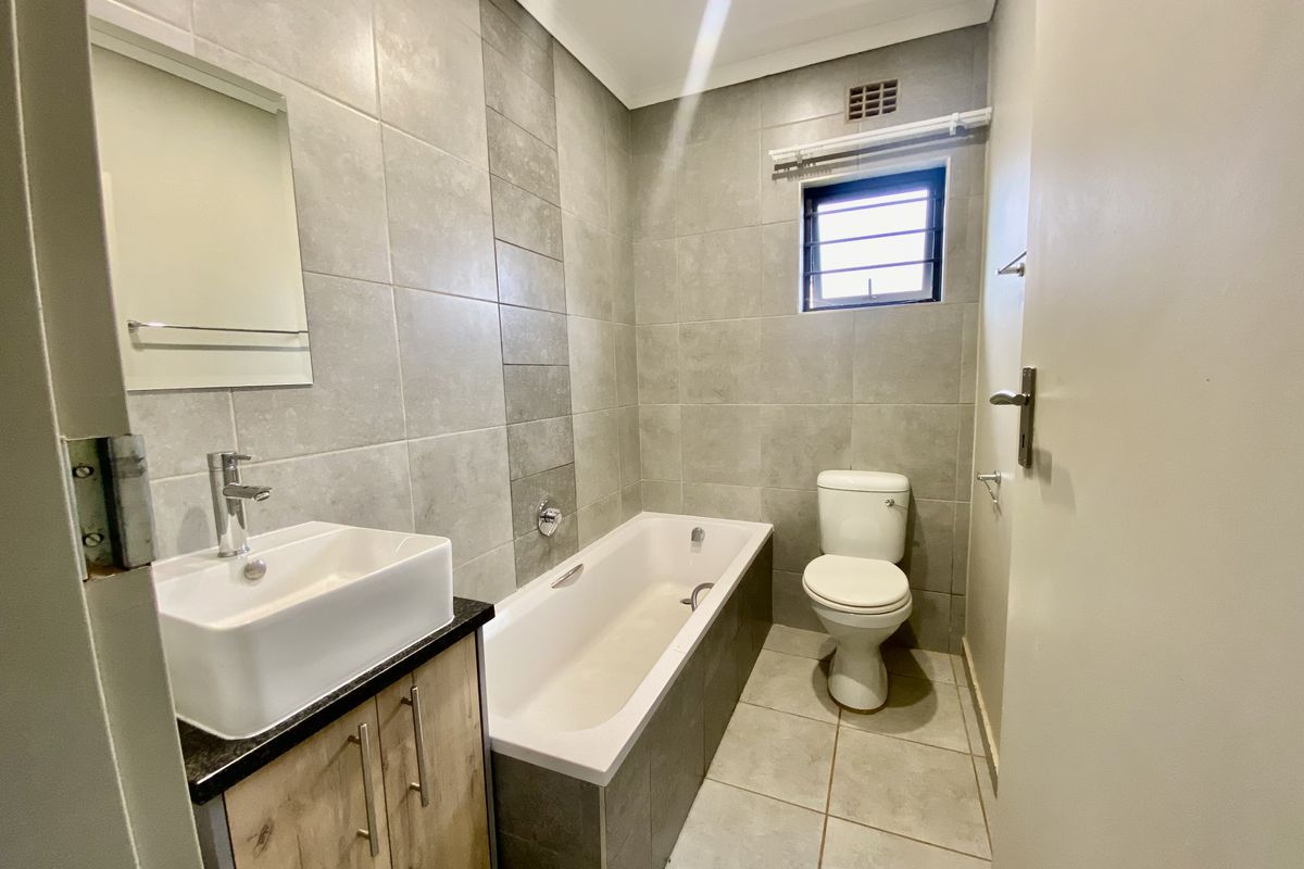 A modern, well-maintained bathroom featuring a vessel sink on a vanity cabinet, a bathtub, and a toilet with neutral grey wall and floor tiles.
