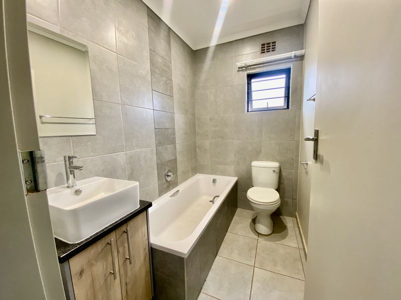 A modern, well-maintained bathroom featuring a vessel sink on a vanity cabinet, a bathtub, and a toilet with neutral grey wall and floor tiles.