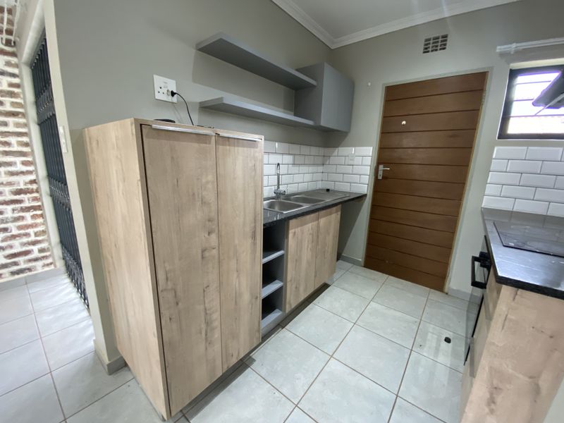A clean and functional scullery area featuring modern wood-look cabinetry, stone countertops, a double sink, and subway tile backsplash.