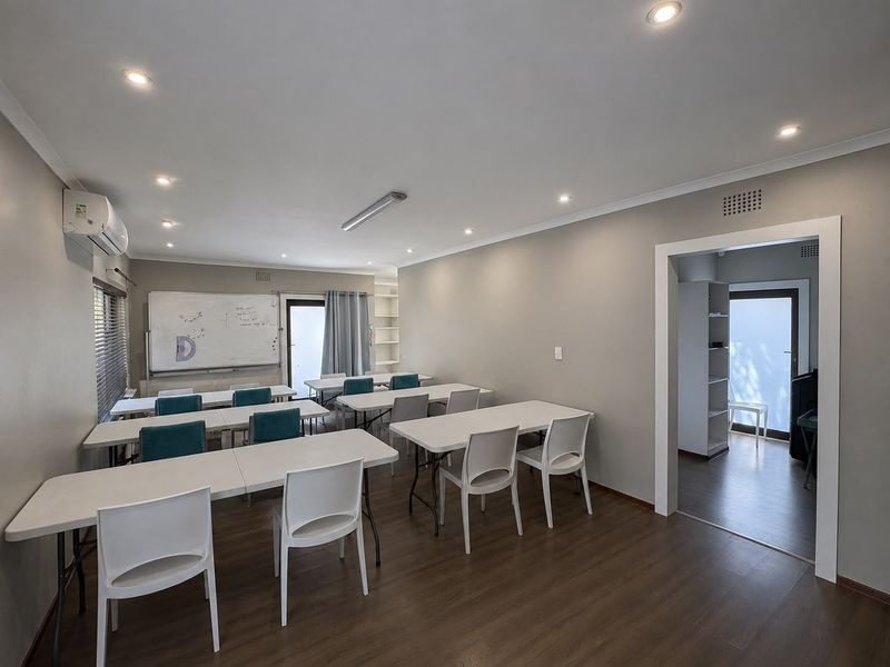 A functional office or training room featuring laminate flooring, recessed lighting, and a split-system air conditioner, with an adjoining secondary space.