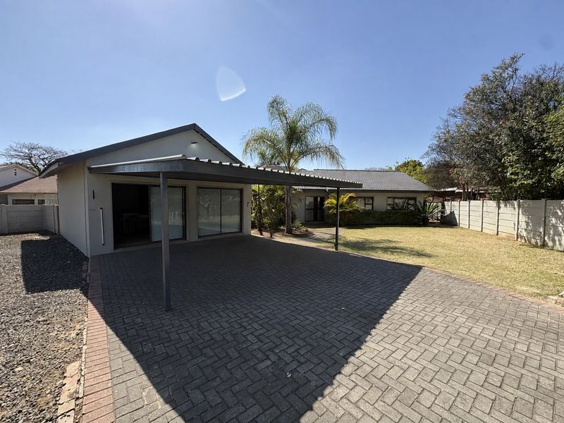 Rear exterior view featuring a paved driveway, a covered carport, and a well-maintained garden area with a precast boundary wall.