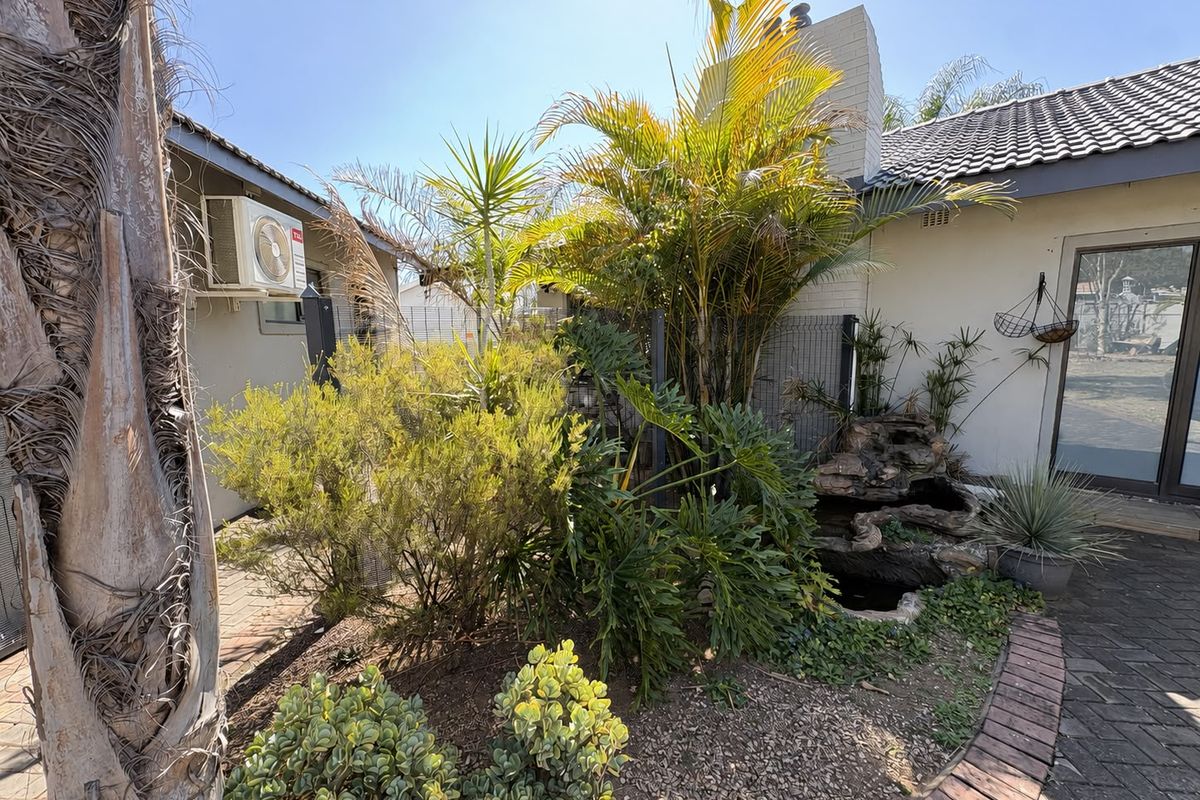 A private rear garden area featuring established landscaping, a small water feature, brick paving, and an exterior air conditioning unit.