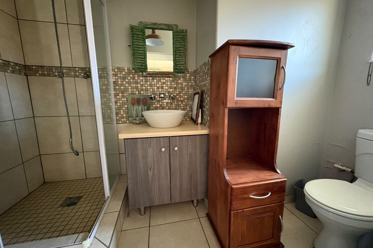 A functional bathroom featuring a shower enclosure, a vessel sink with a mosaic tile backsplash, and a vanity cabinet.