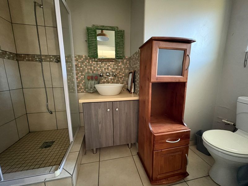 A functional bathroom featuring a shower enclosure, a vessel sink with a mosaic tile backsplash, and a vanity cabinet.